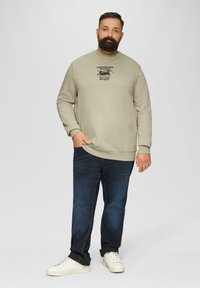 Sweatshirt beige clair avec impression de texte noir sur la poitrine, associé à un jean en denim foncé et des baskets blanches. Coupe décontractée, texture douce.