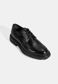 Zwarte leren dress shoe met intrigerende brogue-details, ronde neus en dikke zwarte rubberen zool. Beschikt over een vetersluiting en een gepolijste afwerking.