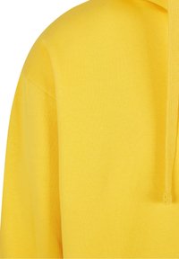 Tissu de sweat à capuche jaune montrant la couture d'épaule, une partie de la manche et le cordon à l'avant.