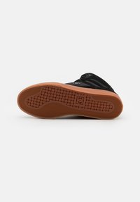 Black sneaker with rubber sole featuring a herringbone pattern, padded collar, and logo accent on the side. Sole is brown with textured grip.