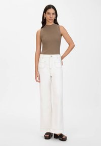 Καφέ ριγέ αμάνικο τοπ συνδυασμένο με λευκό ψηλόμεσο παντελόνι φαρδύ και μαύρες πλατφόρμες με σχέδιο λουριού.