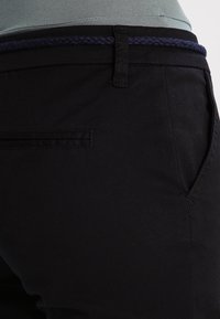 Black trousers made of cotton, featuring a textured braided navy belt, side pocket, and a smooth fabric finish.