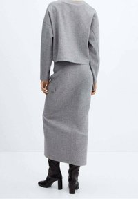 Pull et jupe en mélange de laine grise, avec un design court, des manches longues et une poche latérale, associés à des bottes noires montant jusqu'aux genoux.