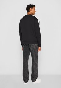 Svart sweatshirt med vit sidopanel, ribbad mudd och nederkant. Bärs med svarta jeans och vita sneakers. Modell vänd bort från kameran.