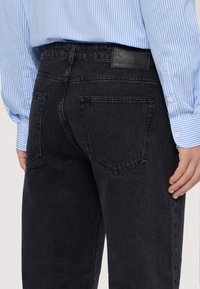 Černé džíny s rovný střih, s zadními kapsami a koženou nášivkou. Nosené s svetrem světle modré barvy s pruhy.