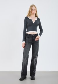 Gray long-sleeve crop top with a white collar, button detailing at the neckline, paired with black wide-leg jeans and black shoes.
