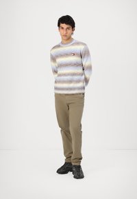 Knitted sweater with light blue, beige, and brown horizontal stripes. Features a round neckline and a small logo on the left chest.