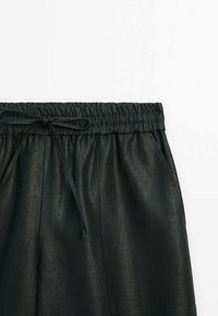 Pantalon noir à cordon avec taille élastique et poches latérales, présenté recadré de la taille jusqu’à mi-cuisse sur un fond uni.