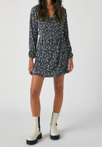 Mekko, jossa on kukkakuosi ja pitkähihaisuus, tummansinisessä värissä, valmistettu kevyestä kankaasta. Mekossa on kerätty vyötärö ja hienovaraisia poimuja, yhdistettynä vaalean kermanvärisiin Chelsea-saappaisiin.