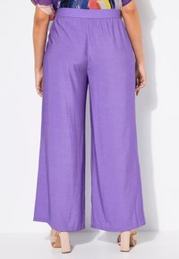 Paarse hoge taille broek met een gladde, lichte stof, voorzien van een elastische tailleband en een recht gesneden ontwerp. Schoenen zijn beige blokhakken.
