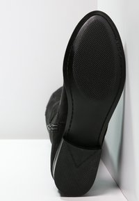 Černé semišové kotníkové boty s texturovanou gumovou podrážkou, bočním zipem a šikmým podpatkem. Viditelné švy dodávají detail po obvodu.