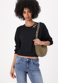 Melna īsā svītera augšdaļa ar apaļu kakla izgriezumu un sudraba acu aksesuāriem. Saskaņota ar gaiši ziliem džinsiem un olīvzaļas zamšādas plecu somu.