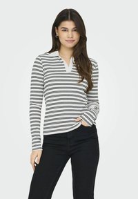 Sort-hvidstribet bluse med lange ærmer, krave og V-hals. Fremstillet af bomuldsstof med en glat overflade, kombineret med mørke jeans.