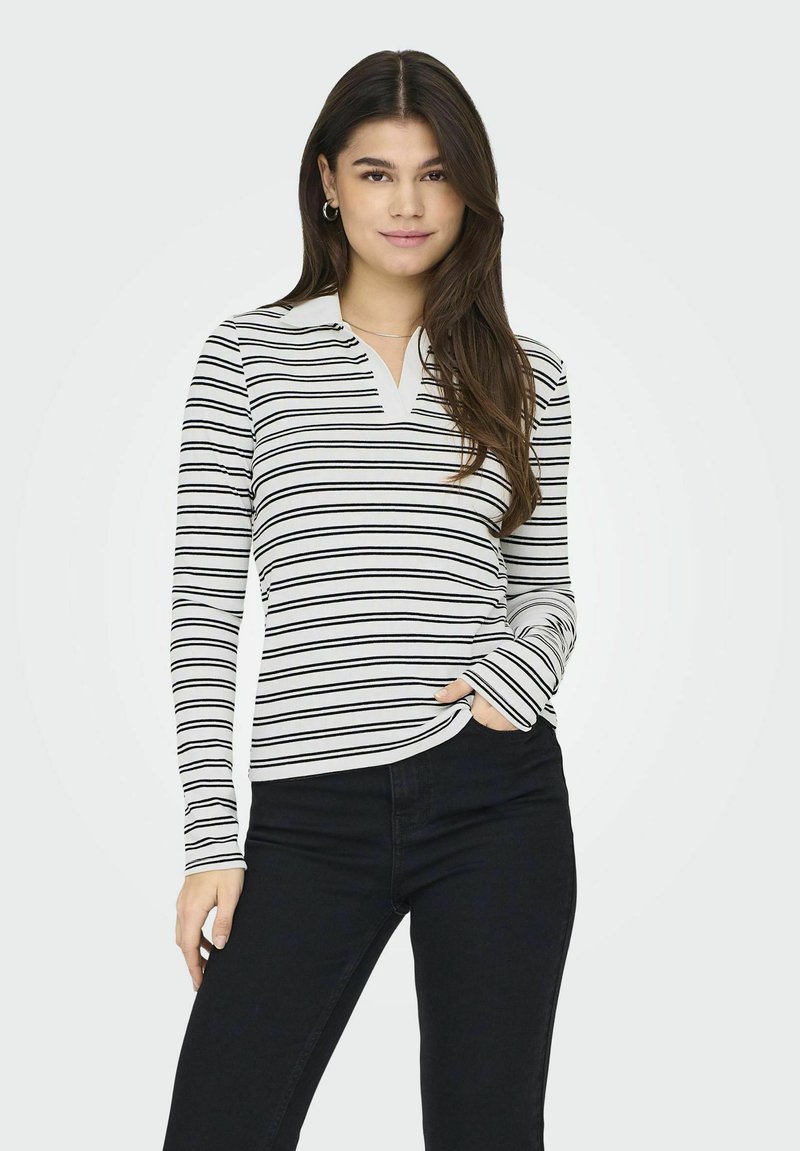 Sort-hvidstribet bluse med lange ærmer, krave og V-hals. Fremstillet af bomuldsstof med en glat overflade, kombineret med mørke jeans.