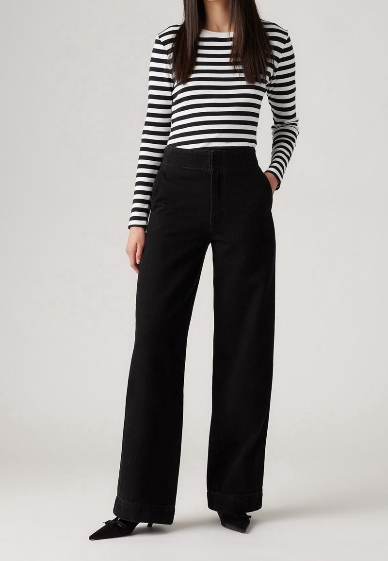 Raidallinen mustavalkoinen pitkähihainen paita, joka on yhdistetty korkeavyötäröisiin mustiin leveälahkeisiin housuihin. Rakennekangas suorassa siluetissa. Mustat kärkitossut.