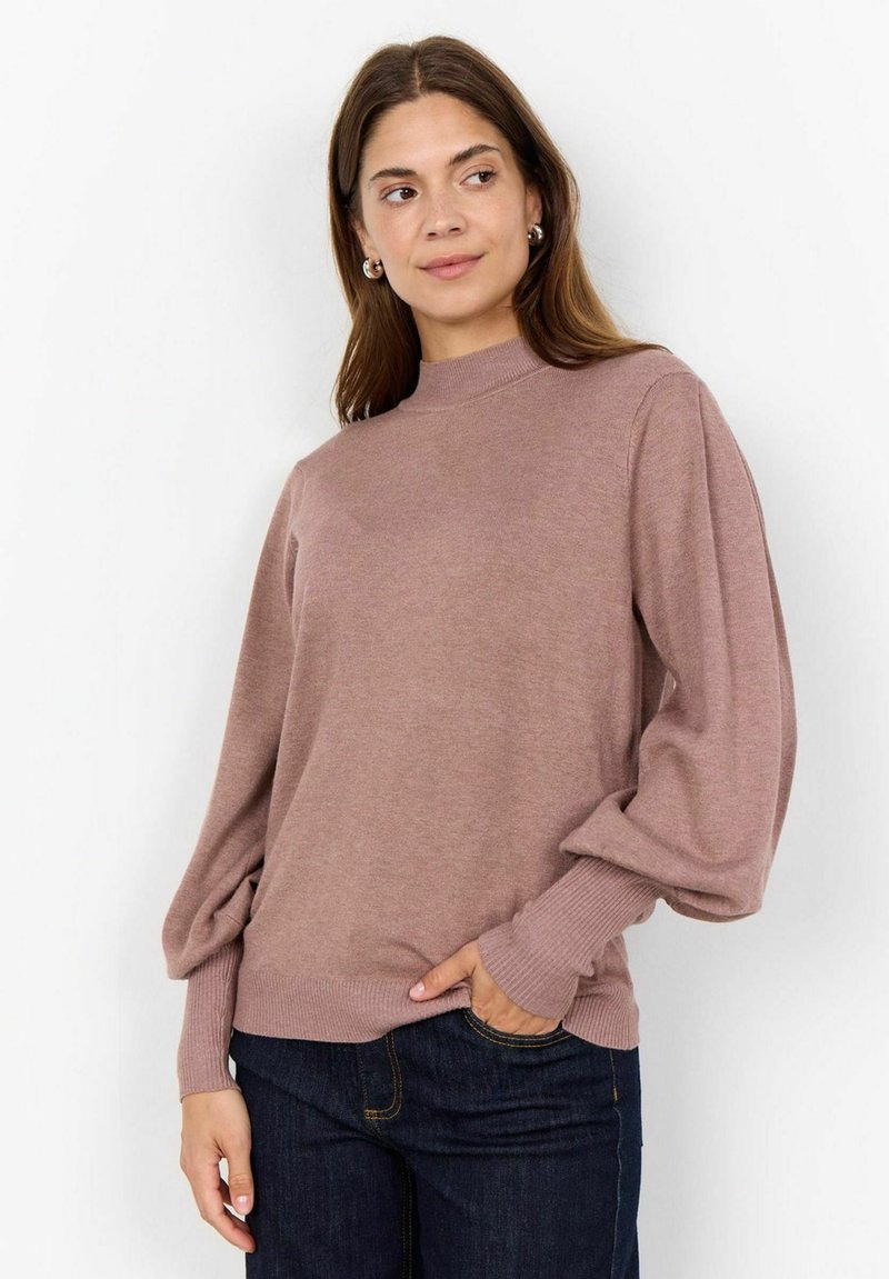 Pull en maille mauve clair avec un col haut, des manches bouffantes longues et des poignet côtelés, associé à un jean en denim foncé.