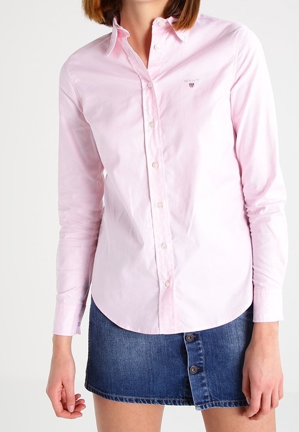 Femme portant une chemise rose clair boutonnée avec col et une mini-jupe en jean bleu avec des boutons à l'avant.