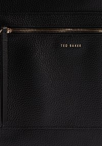 Juoda tekstūruota odinė rankinė su auksine užtrauktuku ir prekės ženklo "TED BAKER" logotipu. Yra lygių akcentų ir paprasto, minimalistinio dizaino.
