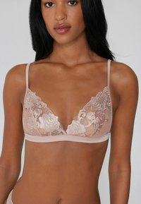 Bralette en dentelle nude avec broderie florale, bonnets triangulaires, fines bretelles et un bandeau élastique lisse. Design léger et transparent.