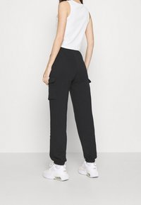 Černé cargo tepláky vyrobené z měkké tkaniny se bočními kapsami, elastickými lemy, v kombinaci s bílým tílkem bez rukávů a bílými teniskami.