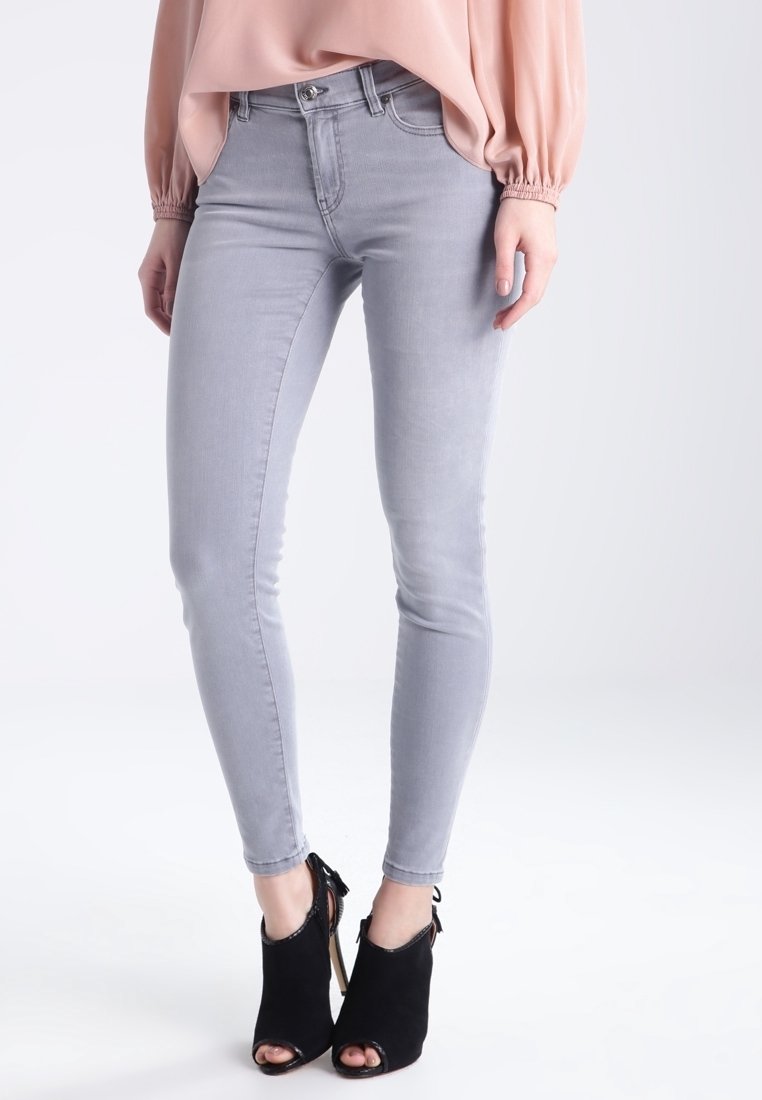 Jean skinny gris en denim, avec une coupe ajustée. Portés avec des bottines à talons ouvertes noires, mettant l'accent sur la texture du tissu et la couleur.