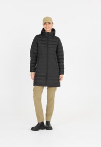 Sort puffetjakke med lynlås foran, hætte og firkantet silhuet. Kombineret med beige cargo-bukser og sorte ankelstøvler. Simpelt design.