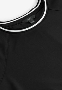 T-shirt noir à col rond avec col côtelé rayé blanc et noir, présentant une étiquette de la marque « NEXT » à l’intérieur du col.