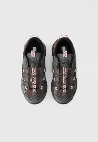 Sport shoes featuring a dark grey mesh upper with pink accents, textured surfaces, and elastic laces. Prominent logo on the tongue.