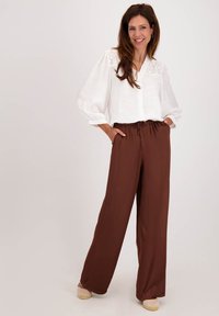 Witte blouse met knoopsluiting en geborduurde details, gecombineerd met hoge taille brown wijde broekspijpen. Zachte stof en een relaxte pasvorm.