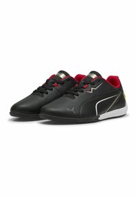 Chaussures de sport noires avec des accents rouges, présentant un design épuré, un matériau perforé pour la respirabilité et une semelle en caoutchouc texturée.