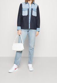 Farkkutakki tummansinisillä ja vaaleansinisillä paneeleilla, kahdella rintataskulla, yhdistettynä vaaleansiinisiin farkkuihin ja valkoiseen käsilaukkuun. Valkoiset lenkkarit punaisilla yksityiskohdilla.