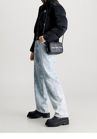 Giacca a piumino nera, jeans a gamba larga a lavaggio acido azzurro chiaro, stivali piattaforma neri e una piccola borsa a tracolla nera Calvin Klein.