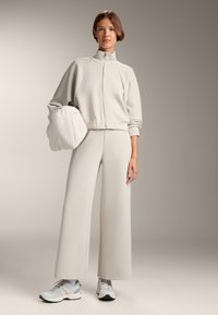 Vaalea harmaa urheiluasu, jossa on vetskari takki ja leveälahkeiset housut, valmistettu ribbikankaasta. Yhdistettynä valkoisiin lenkkareihin. Pehmeä rakenne.