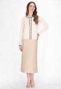 Beiges Kleid mit taillierter Taille und fließendem Rock, kombiniert mit einer cremefarbenen, geknöpften Strickjacke mit schwarzem Saum und langen Ärmeln.