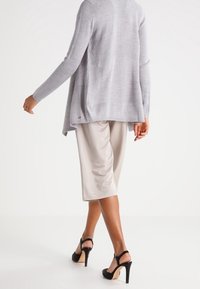 Cardigan en tricot gris clair à coupe ample, associé à un pantalon large beige et des sandales à talons noirs, vu de dos.