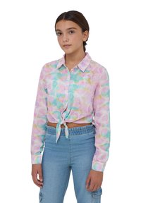 Camicia accorciata con nodo anteriore in tonalità pastello di rosa, turchese e giallo, con colletto a bottone e maniche lunghe. Indossata con jeans a vita alta.