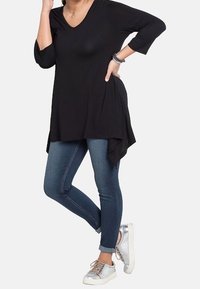 Musta, kolme neljänneksen hihalla varustettu tunika, jossa on V-kaula-aukko, yhdistettynä tiukkoihin farkkuihin. Mallilla on päällään hopeiset lenkkarit ja kerrokselliset rannekorut.