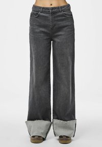 Breda jeans i mörkgrå denim med rå kant och gråa detaljer. Har en klassisk femfickorsdesign och en dragkedja med knappstängning.