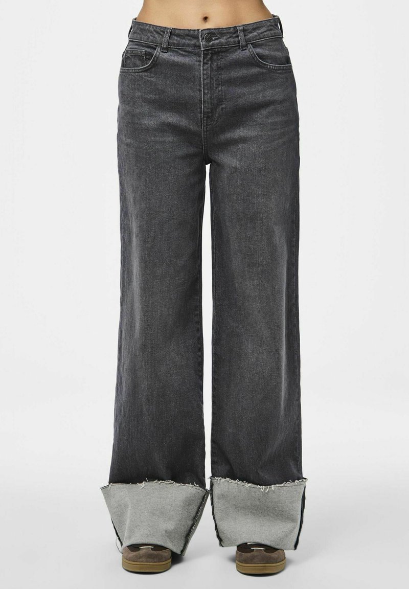 Breda jeans i mörkgrå denim med rå kant och gråa detaljer. Har en klassisk femfickorsdesign och en dragkedja med knappstängning.