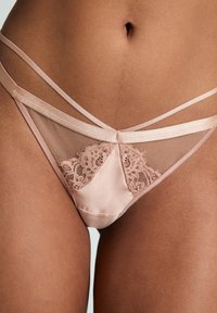 Naakt lingerie met een doorschijnend gaaspaneel en decoratieve kantdetails. Satijnen banden zorgen voor een gestructureerd ontwerp. Zachte textuur, minimale bedekking.