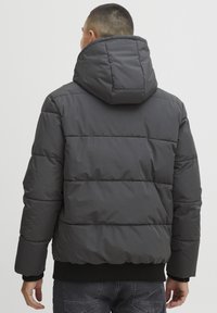 Puffer jacket in dark gray with a hood, featuring a quilted design, ribbed cuffs, and hem, showcasing a smooth, shiny texture.
