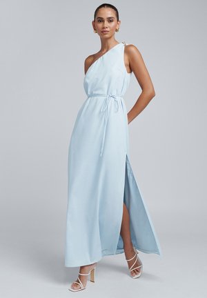 Lyseblå maxikjole med enkelt skulderstrop, bånd i taljen, højt slid og dekorativt hardware på skulderen. Glat tekstur og flydende design.