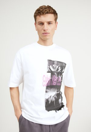 Vit bomull t-shirt med ett svartvitt grafiskt tryck och rosa text. Korta ärmar, avslappnad passform och rund halsringning.