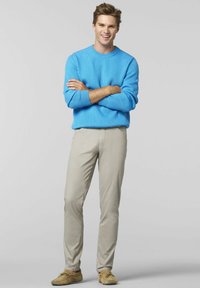 Hellblau gestrickter Pullover mit Rippmuster, beiger Slim-Fit-Hose und sandfarbenen Mokassins. Das Model steht mit verschränkten Armen und lächelt vor einem grauen Hintergrund.
