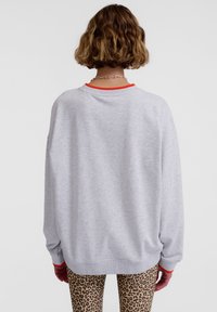 Grå oversize sweatshirt med röd krage, har en avslappnad passform och långa ärmar, matchad med leopardmönstrade leggings.