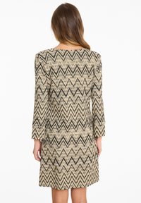 Knielanges Kleid mit Zickzack-Muster in Beige und Schwarz, mit langen Ärmeln und geradem Schnitt. Hergestellt aus strukturierter Stoff.