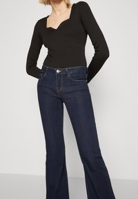 Svart ribbad body med fyrkantig halsringning, kombinerad med mörkblå utsvängda jeans med framfickor och subtila sömnadsdetaljer.