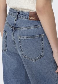 Blå denimjeans med hög midja, synlig söm, två bakfickor och en brun läderetikett med texten "ONLY" på midjebandet.