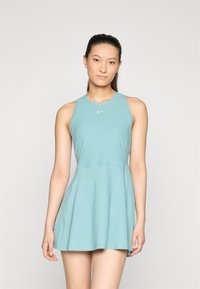 Um vestido atlético em teal claro com parte superior justinha e saia rodada. Apresenta um design sem mangas e um logo da Nike em branco no peito.