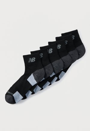 Seks par sorte og grå New Balance ankelstrømper arrangeret i en række på en hvid baggrund.